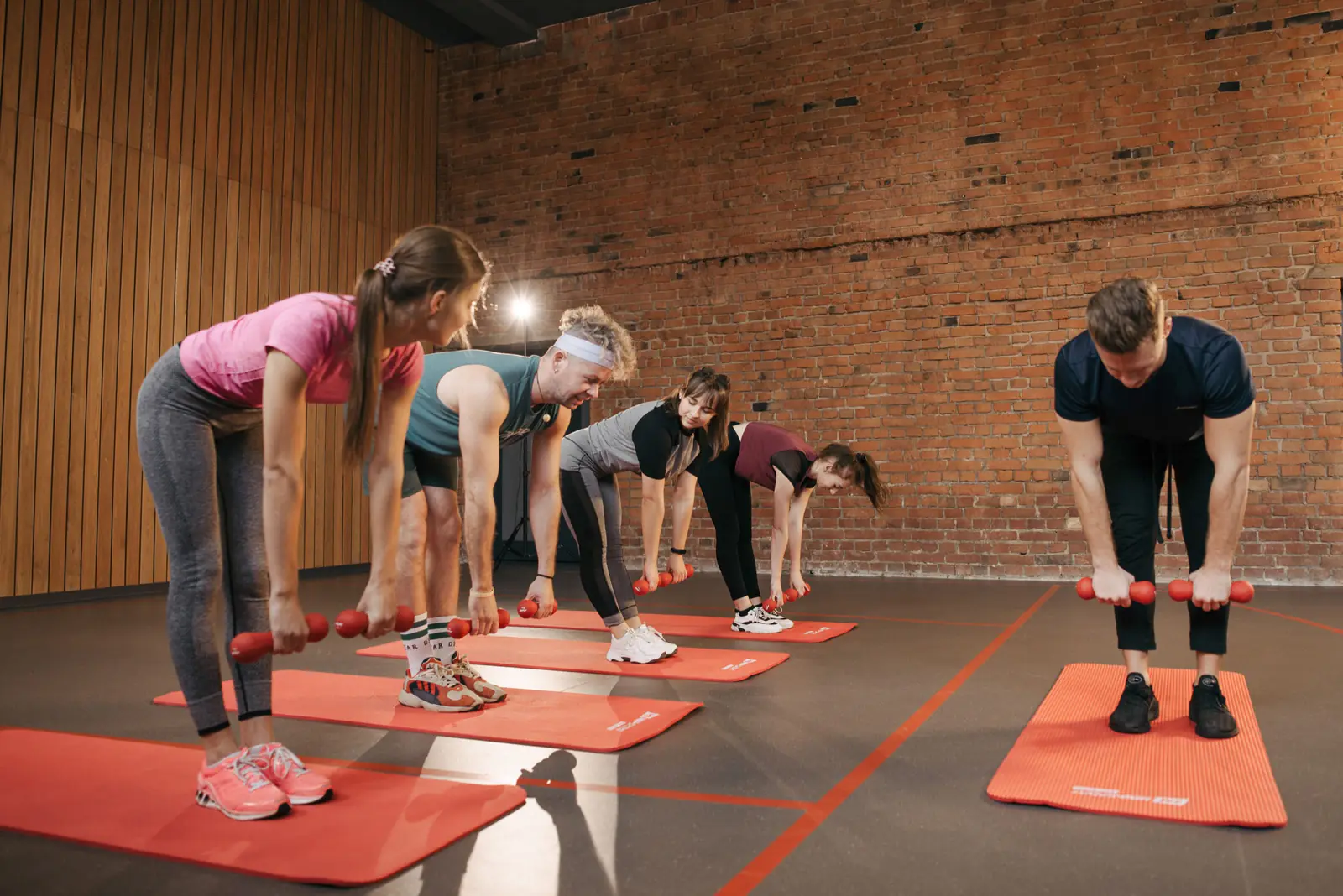 A coach leading four members through a dumbbell row on red mats in a brick and timber studio